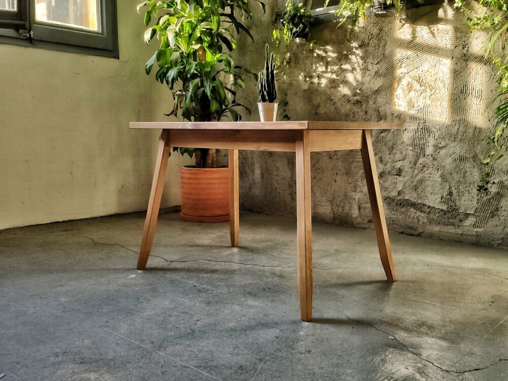 Mesa de madera maciza Dyrån que decora un salón con una pared de cemento y varias plantas que potencian la luminosidad